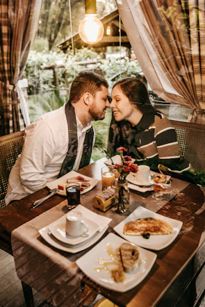 Close-up of a couple holding hands over a breakfast tray filled with croissants, strawberries, and a small bouquet.