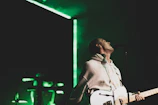 Young Mexican musician passionately playing guitar on stage with vibrant green lighting.