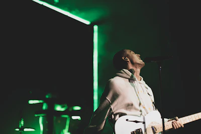 Young Mexican musician passionately playing guitar on stage with vibrant green lighting.