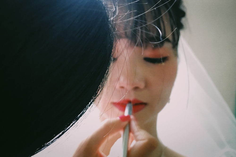 person applying lipstick on woman wearing wedding veil