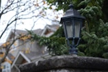 Elegant outdoor lantern mounted on a rustic iron post surrounded by greenery.