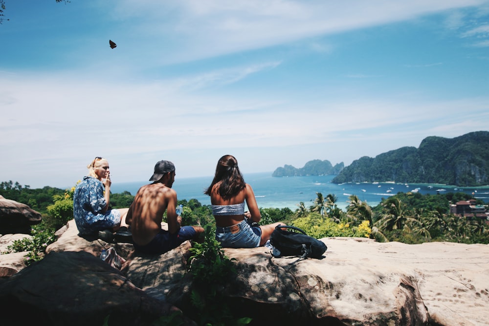 topless man sitting between two persons near body of water