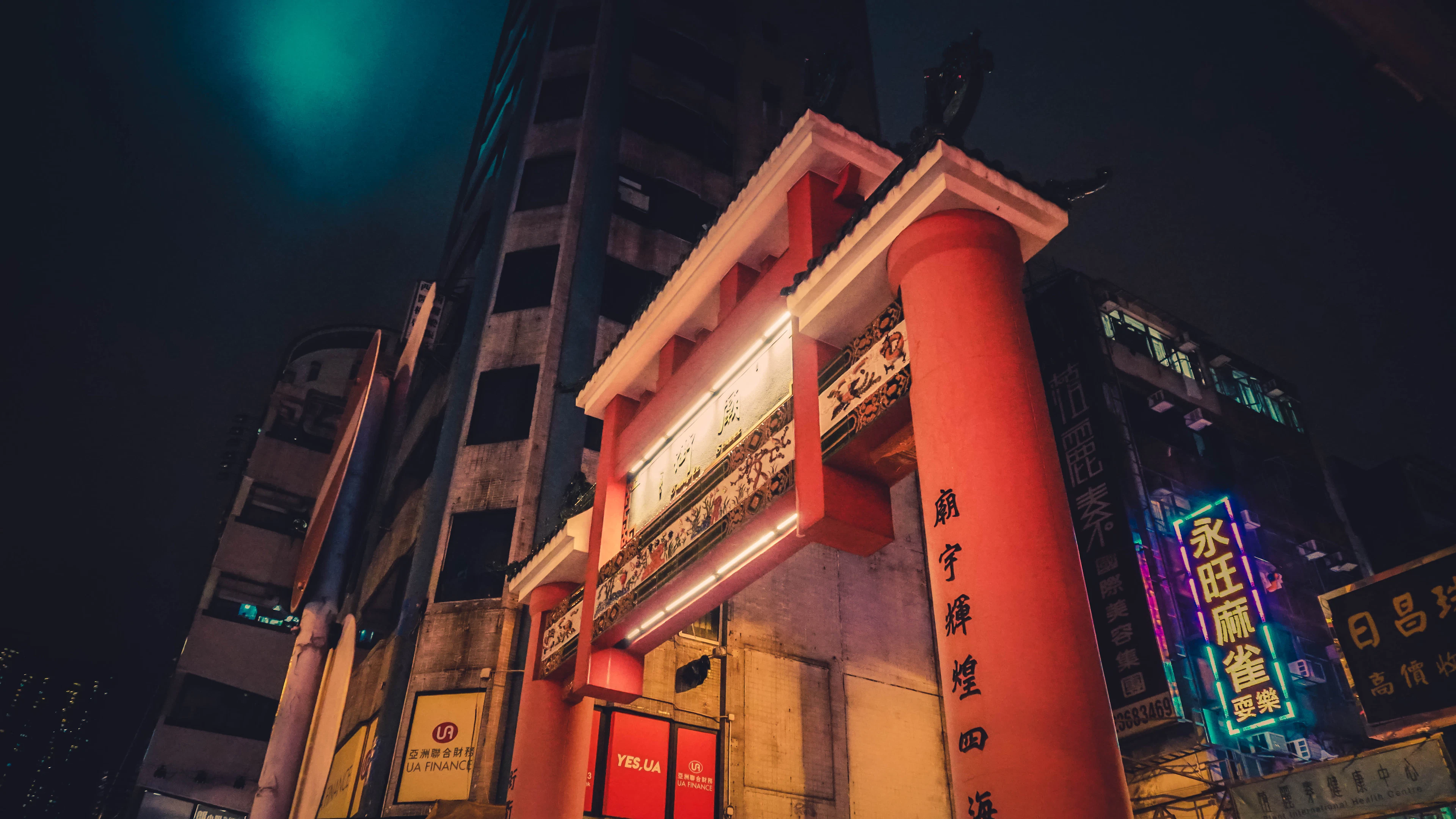 A red temple gate lit at night beneath a wall of neon signs in Kowloon, Hong Kong.