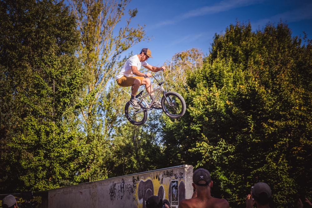 man wearing white crew-neck t-shirt doing stunts using black bike surrounded with people watching under blue and white sky during daytime