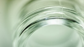 A close-up of a glass jar focusing on its rim, highlighting the transparent and glossy texture. The soft lighting creates a gentle reflection on the glass surface.