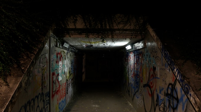 A dimly lit tunnel entrance with faint graffiti, hinting at stories beneath the city streets.