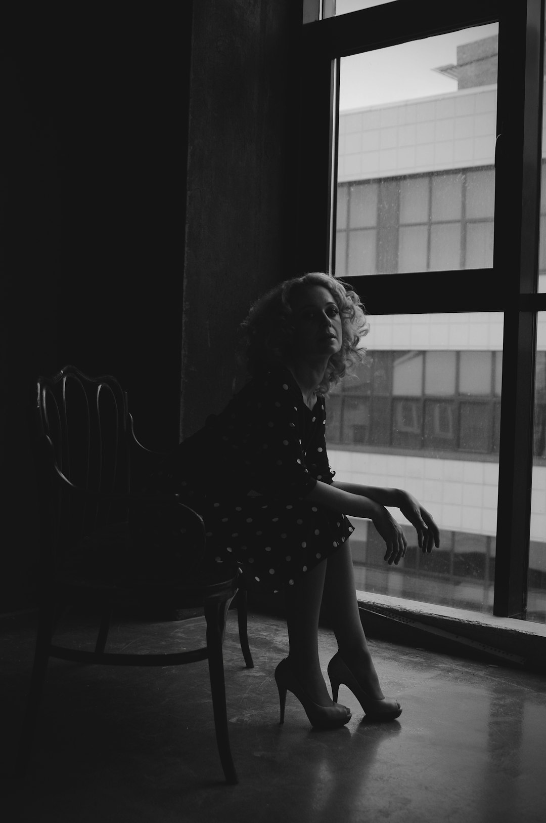 grayscale photography of woman sitting near glass window