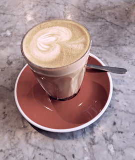 A hand holding one of our elegant coffee spoons, poised over a frothy latte in a cozy café setting.