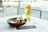 A glass of Heineken beer sits next to a black bowl filled with chicken wings and a dipping sauce on a table. The setting appears to be a cafe or restaurant with large glass windows overlooking an outdoor area.