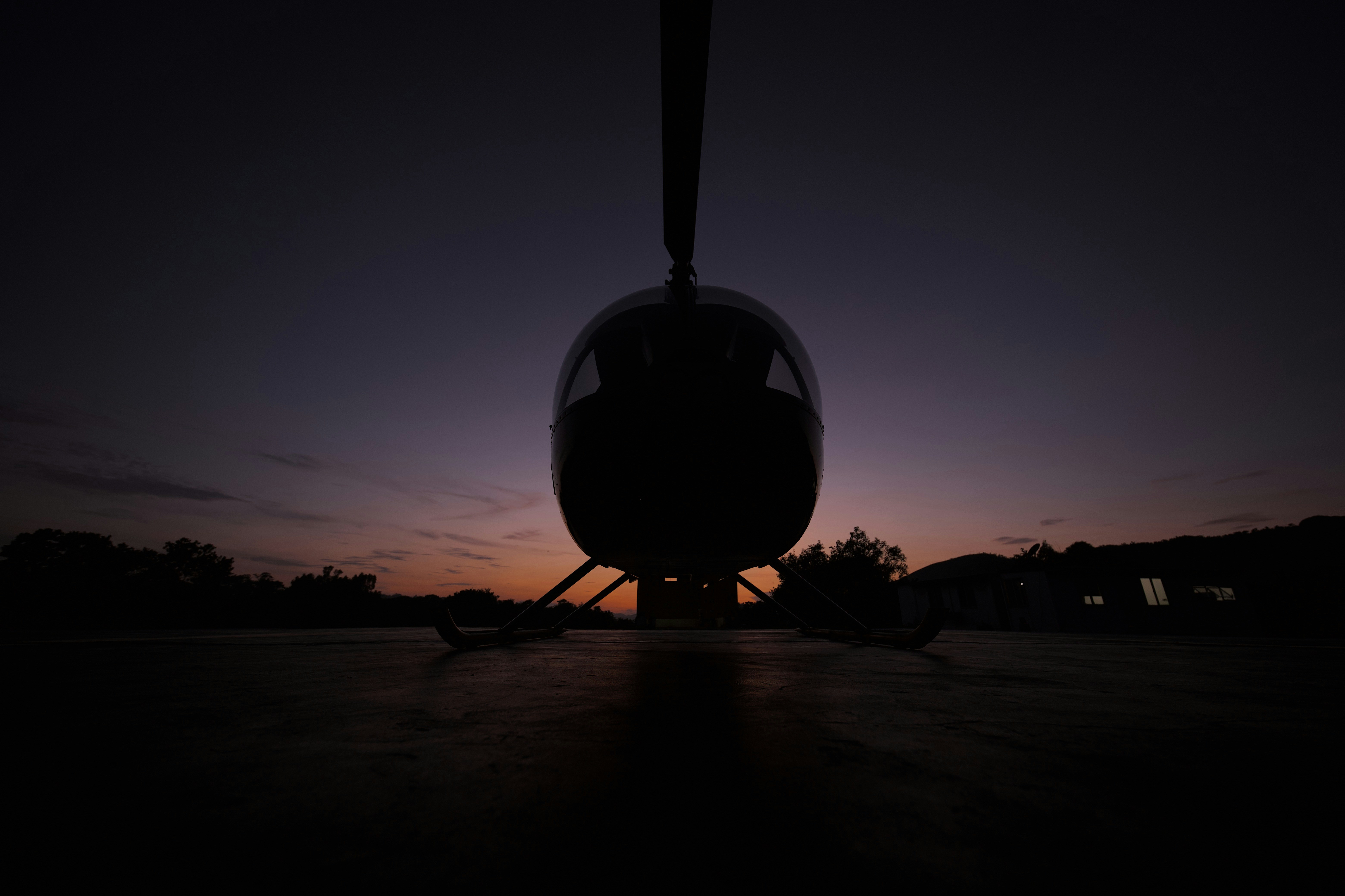 A helicopter parked on a concrete landing pad at sunset.