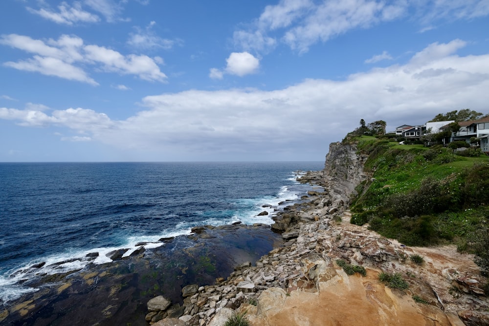 rocky cliff facing ocean under blue cloudy sky