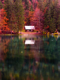 A serene lakeside cabin reflecting on calm waters surrounded by autumn trees