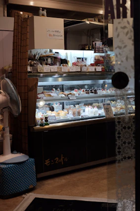 A cozy bakery counter displaying an assortment of colorful cakes and sweets under warm lighting.