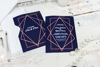 Stack of printed graduation invitations with black, white, and gold accents on a wooden table.