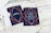 Wedding invitations are placed on a rustic white wooden table. The invitations feature a navy blue background with elegant geometric designs in rose gold. One card displays the words 'Future Mr & Mrs,' while the other provides details about the wedding, including names and the date. Nearby are a pen, an envelope, and some string lights, creating a warm and inviting atmosphere.
