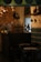A vintage-style interior decorated with dark wooden furniture, an old radio, and a vintage fan. The walls have a rustic design with brickwork and antique light fixtures. Shelves hold various decorative vases and teapots, adding to the classic ambiance.