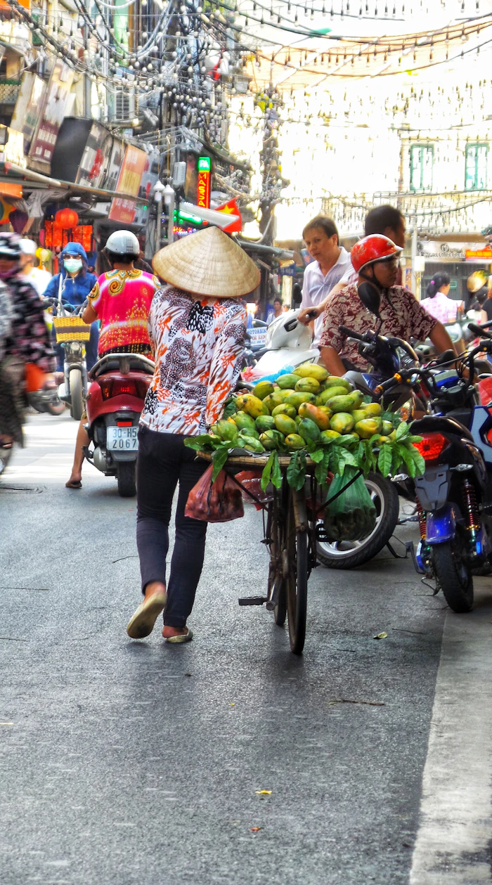 Vendedora con sombrero cónico y una bicicleta cargada de frutas en una calle de Asia