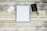 A flat lay of a stationary set featuring a stack of blank white paper placed in the center, surrounded by a pen with a polka-dot pattern, a few white envelopes, a black envelope with gold trim, and a metallic gold stapler all arranged on a rustic wooden surface.