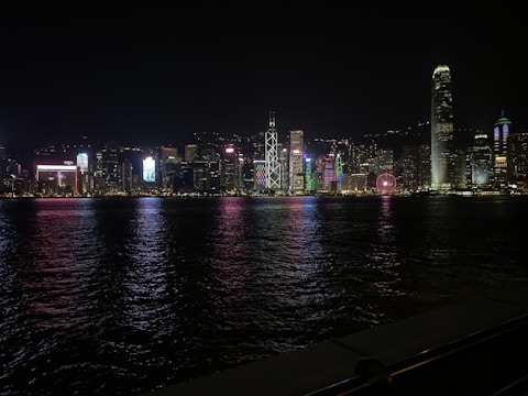 A bustling city skyline at night illuminated by colorful lights reflecting on a river.