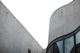 A modern architectural structure with a focus on geometric lines and smooth curves. The building exterior features large, textured stone tiles and expansive glass windows, conveying a sense of minimalistic elegance.