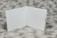 An open book with blank white pages is displayed on a textured gray background. A small gold binder clip is attached to the right side of the book's cover.