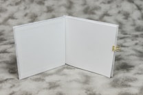 An open book with blank white pages is displayed on a textured gray background. A small gold binder clip is attached to the right side of the book's cover.