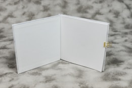 An open book with blank white pages is displayed on a textured gray background. A small gold binder clip is attached to the right side of the book's cover.