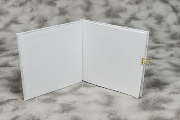 An open book with blank white pages is displayed on a textured gray background. A small gold binder clip is attached to the right side of the book's cover.