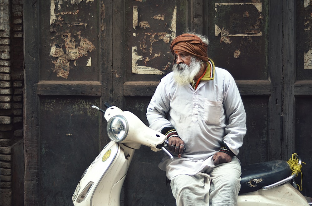 man in white shirt and pants leaning on white motor scooter