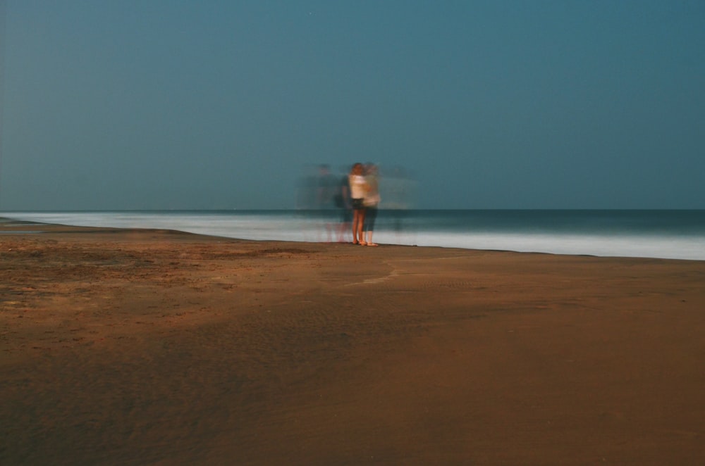 um par de pessoas em pé em cima de uma praia de areia