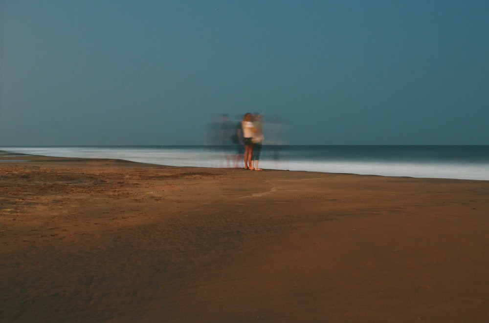 a couple of people standing on top of a sandy beach