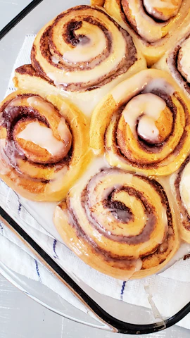 Warm, golden-brown cinnamon rolls drizzled with creamy icing on a white plate.