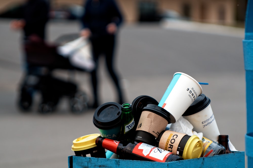 pile of disposable cups and glass bottle on trash can