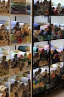 A collection of folded sarees showcasing diverse textures and colors on a wooden shelf.