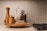 A kitchen countertop features a wooden cutting board holding a variety of kitchen items, including pepper mills, olive oil dispensers, and a small wooden container. The scene is set against a background of tiled wall with a neutral color palette.