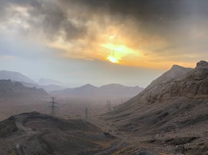 A rugged mountainous landscape with drilling rigs silhouetted against a dusky sky.