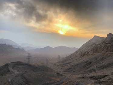A rugged mountainous landscape with drilling rigs silhouetted against a dusky sky.