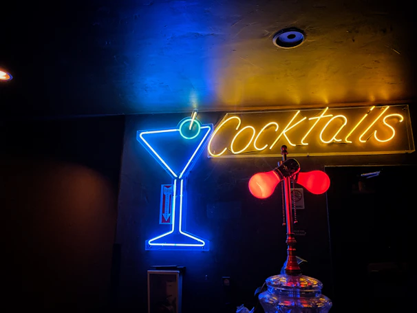 Close-up of colorful cocktails illuminated by electric blue and glowing gold neon lights.
