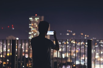 man standing in the terrace taking pictures of citylights