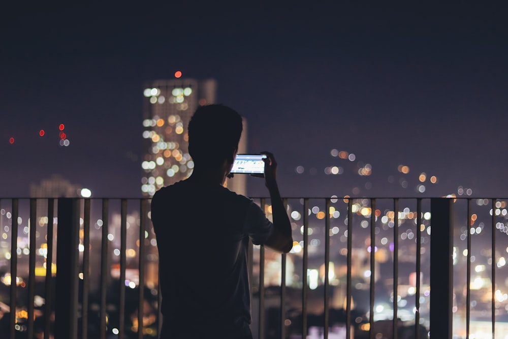 man standing in the terrace taking pictures of citylights