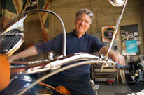Smiling middle-aged man standing beside a sleek outboard engine display in a modern marine showroom.