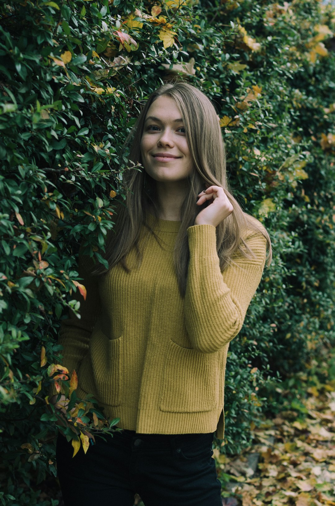 smiling woman wearing brown crew-neck sweater standing beside plants