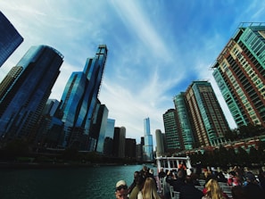 A group of friends laughing on a sleek boat cruising past the Mumbai skyline under clear blue skies.