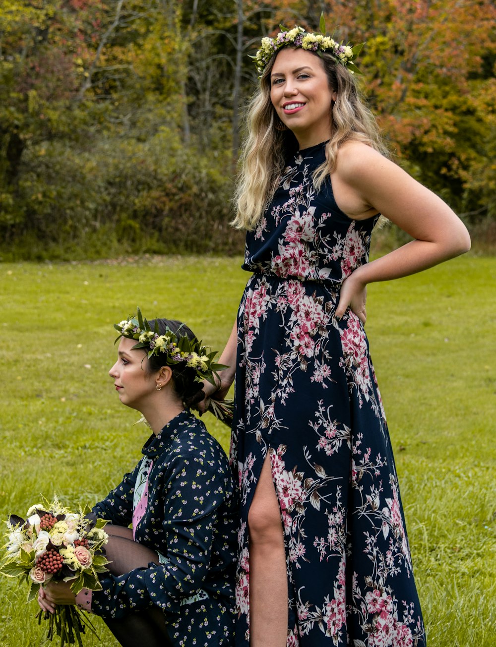 donna che indossa maxi abito floreale accanto alla donna seduta sul campo di erba verde