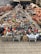 A vibrant display of handmade pottery is arranged on the ground. The collection includes a wide variety of colorful ceramic dishes, bowls, and traditional tagine pots. Shelves and stacked arrays of earthenware line the sides, offering a rich assortment of designs and patterns. The setting appears to be an outdoor market with a mix of small and large clay products neatly organized for sale.