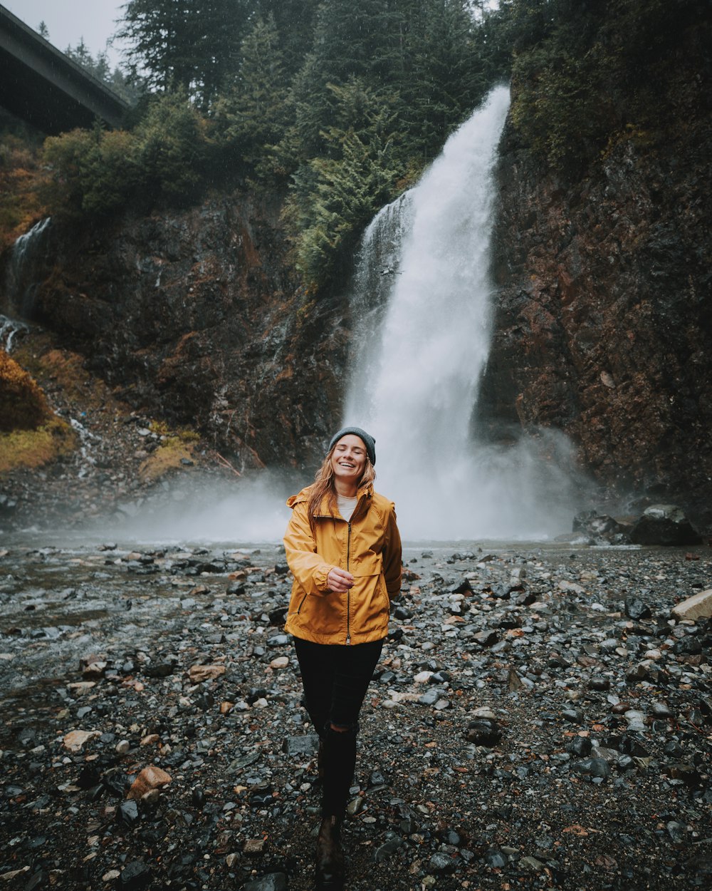 Mujer sonriente de pie cerca de las cascadas durante el día