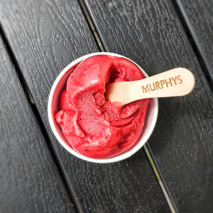 A close crop of a paper cup of sorbet with a small spoon resting in it