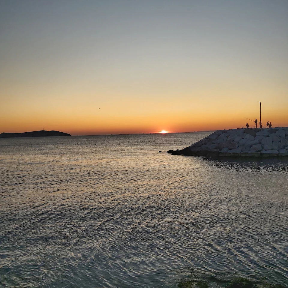 Serene sunset over ocean with sun setting behind horizon, casting warm glow across sky
