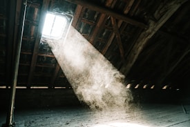 Close-up of hands fitting insulation material inside an attic with natural light