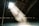 Sunlight streams through a small window in the roof of an attic, casting a soft, illuminating beam that highlights the dust particles floating in the air. The wooden beams of the ceiling are visible, and the space has an aged, rustic feel.